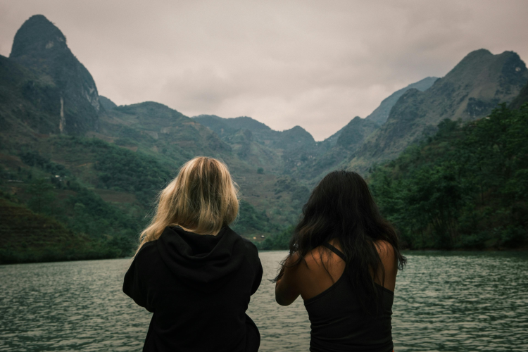Image of mixed race, same-sex couple at a lake with mountains in the background